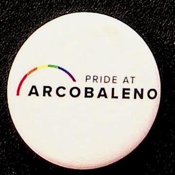 White circular badge with black font reading "Pride at Arcobaleno" and a rainbow graphic.